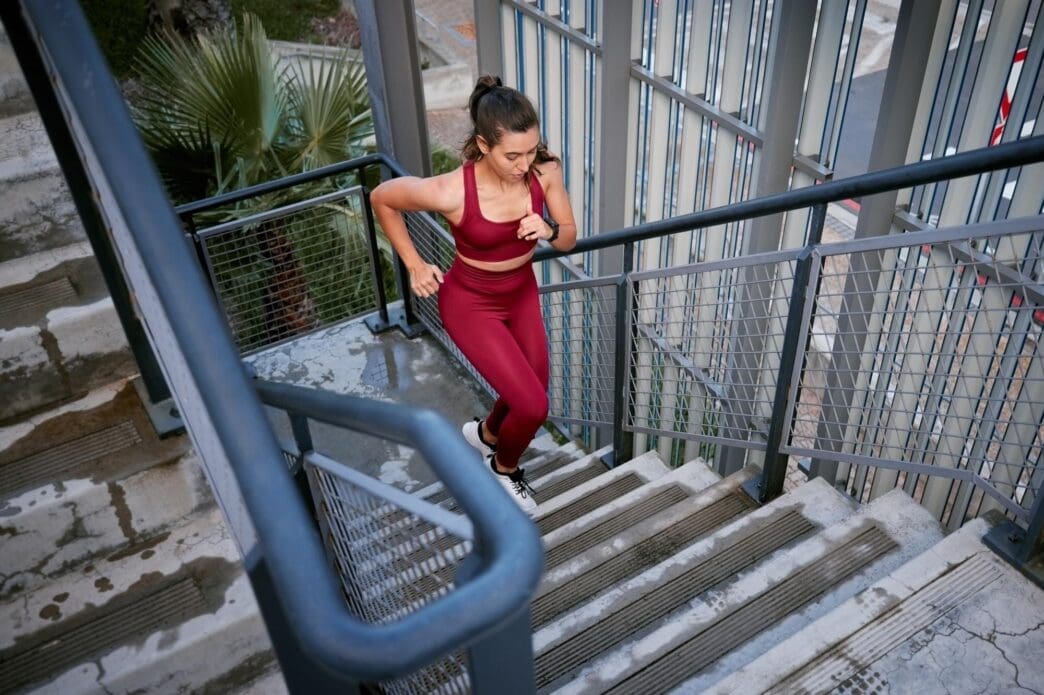 A woman runs up a set of outdoor stairs in a city setting, likely training for a marathon or fitness challenge.