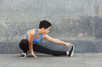 A young woman in workout clothes stretches her legs outdoors, preparing to run.