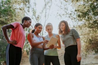 A group of women, engaged in an outdoor activity, are looking at a digital tablet.