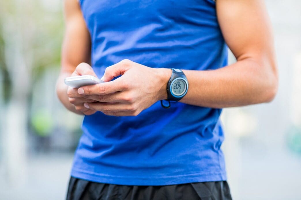 A muscular athlete with short hair looks down at his phone.