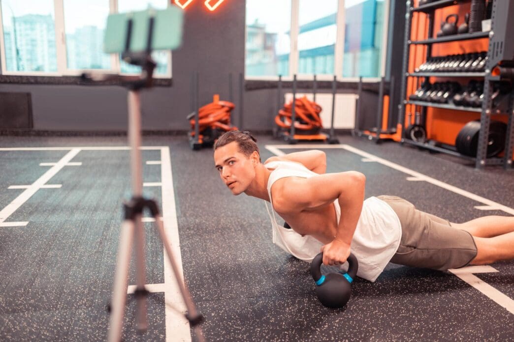 A muscular man with short hair is doing pushups in front of a camera.