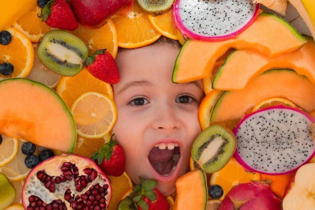 Close-up of a child's face as they eat a variety of colorful fruits.