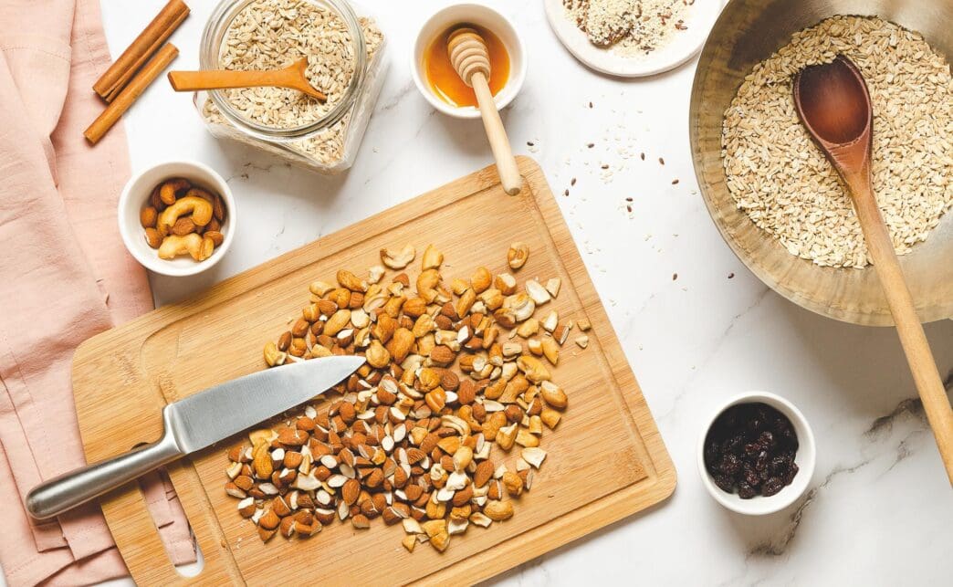 An assortment of nuts, oatmeal, seeds, and honey are arranged on a surface, representing ingredients for homemade granola.