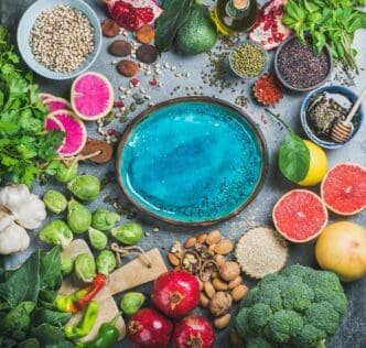 A bright blue plate in the center holds various healthy foods against a grey background.