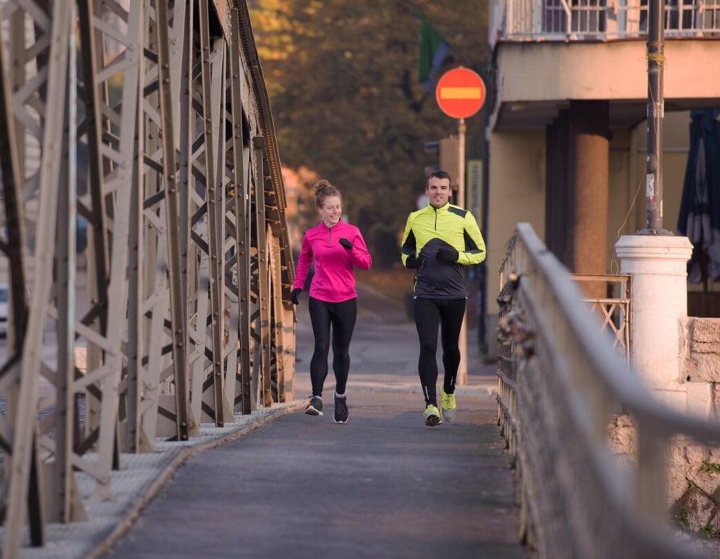 A young couple jogs through a city street at sunrise.