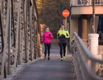 A young couple jogs through a city street at sunrise.