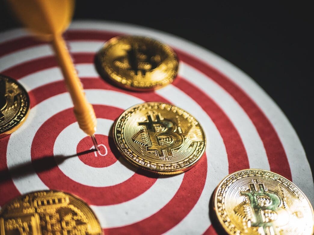 High-angle shot shows a dart piercing a Bitcoin on a black background.