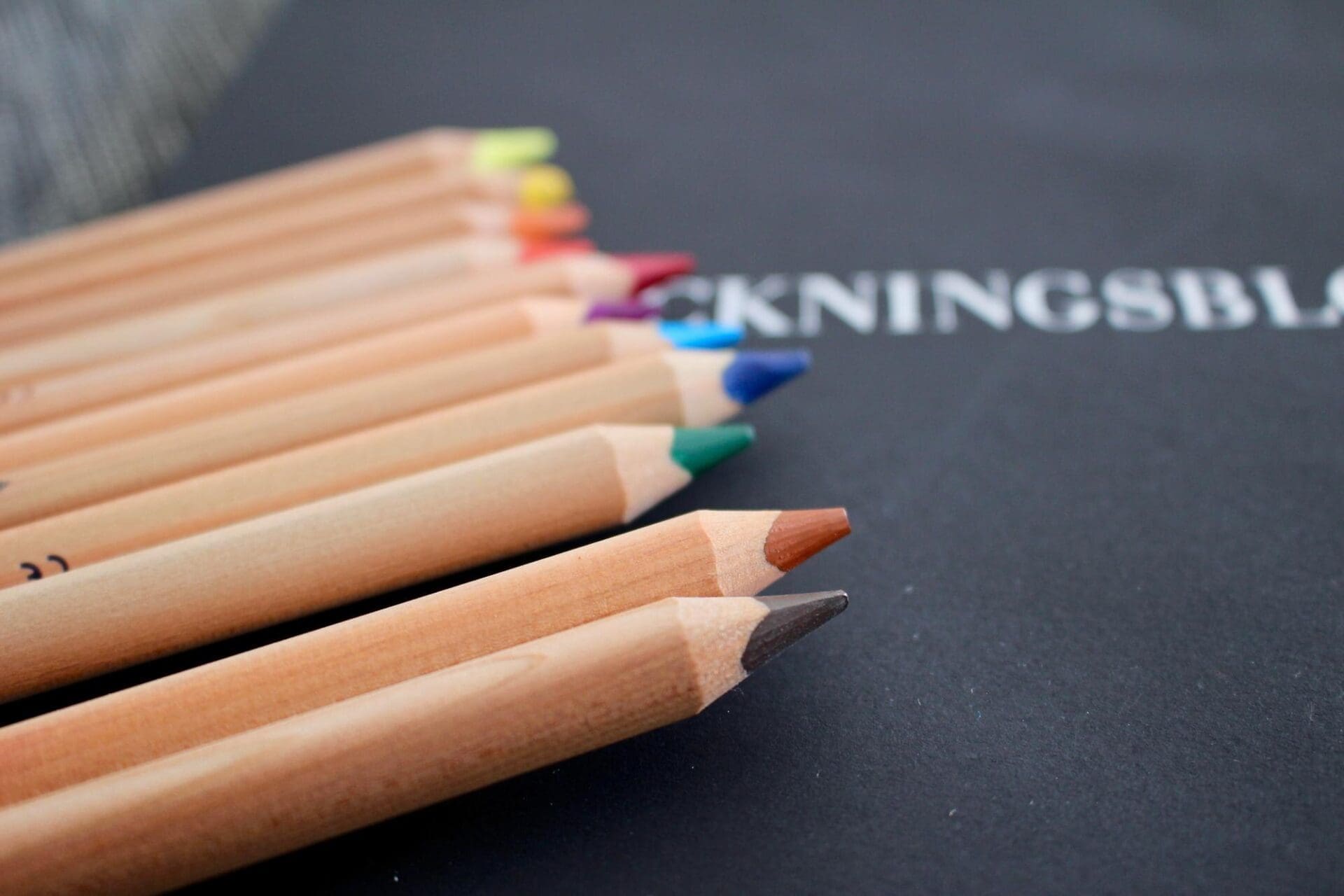 High-angle shot shows a collection of wooden colored pencils scattered on a black chalkboard.