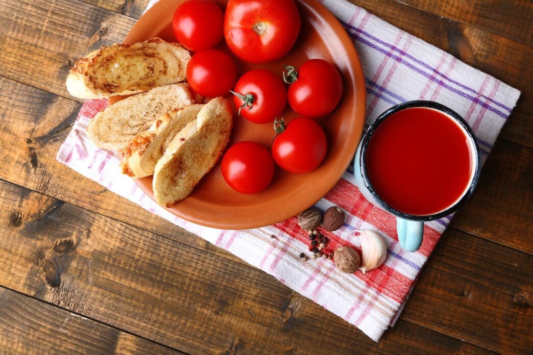 A colorful mug of homemade tomato juice is pictured with fresh tomatoes on a wooden surface.