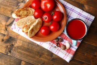 A colorful mug of homemade tomato juice is pictured with fresh tomatoes on a wooden surface.