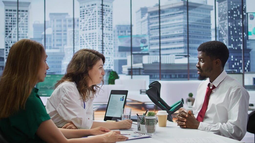 A team of HR recruiters interviews a candidate using crutches in a modern office setting.