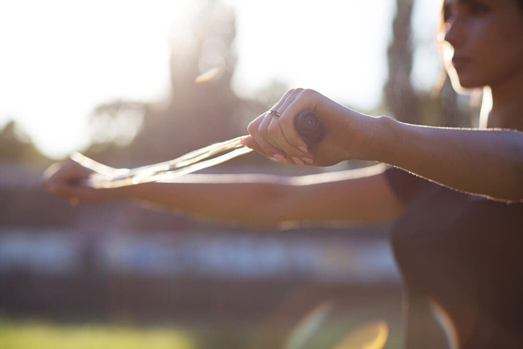 A woman in fitness attire stretches with a jump rope on a stadium track.