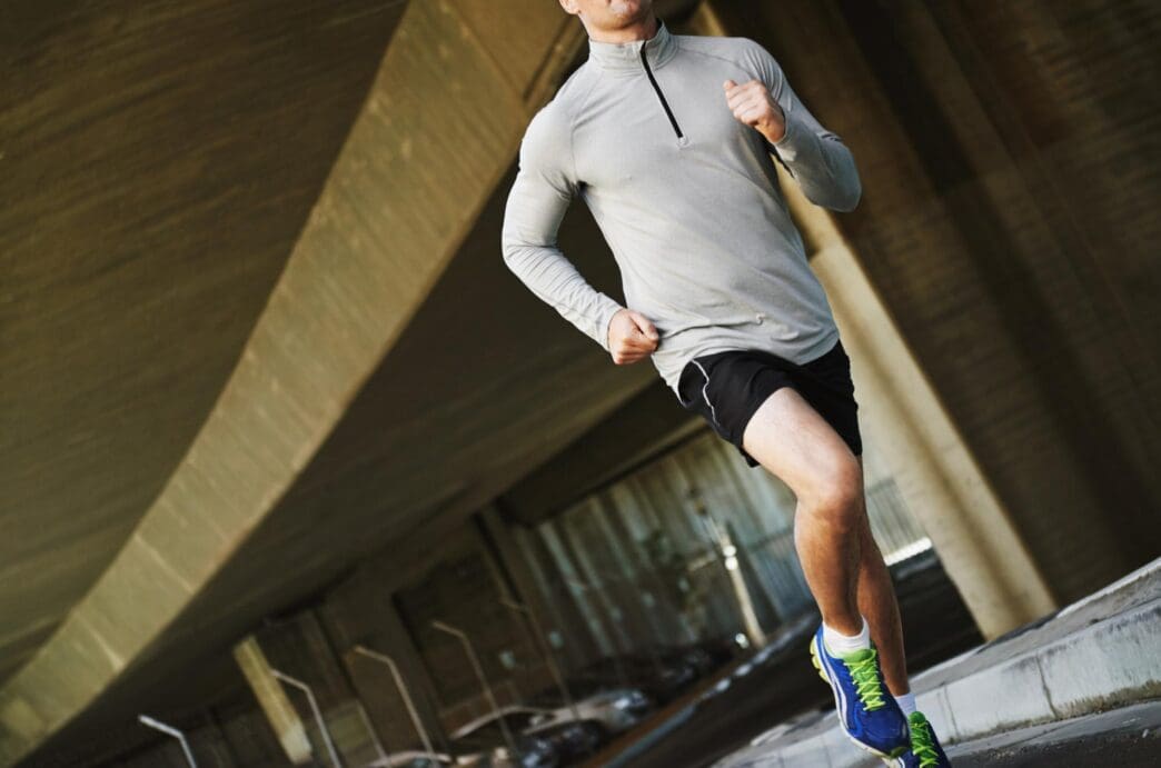 A man in sportswear runs outdoors, likely training for a marathon, with a city bridge in the background.