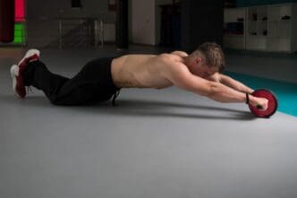 A man is exercising with an ab roller on a floor.
