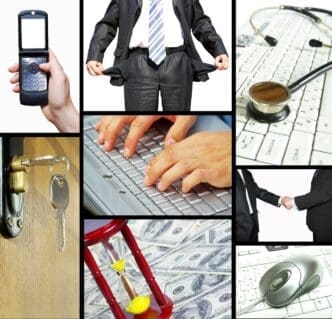 A man sits at a desk, working on a computer and holding a phone.