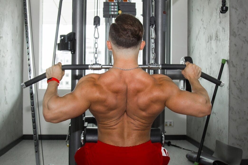 A muscular man lifts weights in a gym, engaging in a weightlifting exercise.