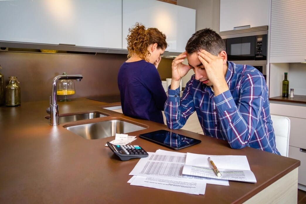 Two men are sitting on a table in a home setting.