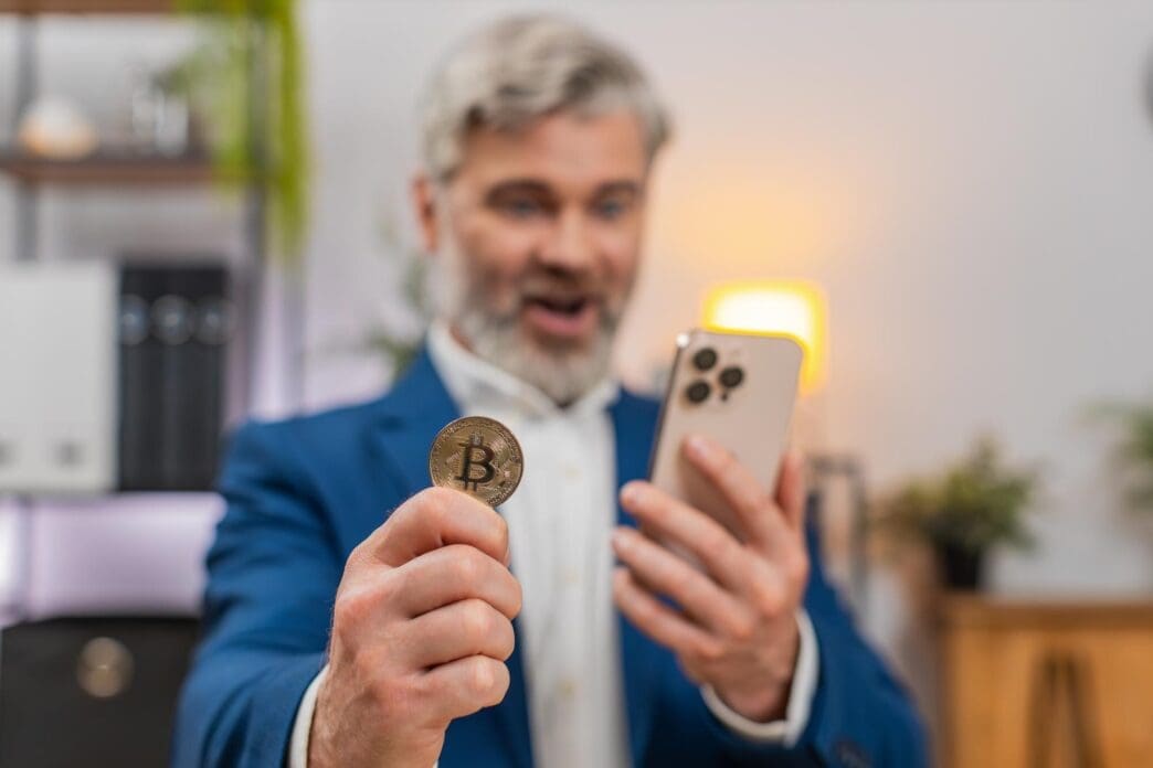 Middle-aged businessman, excited by a Bitcoin rally, gestures with enthusiasm while looking at a crypto app on his smartphone.
