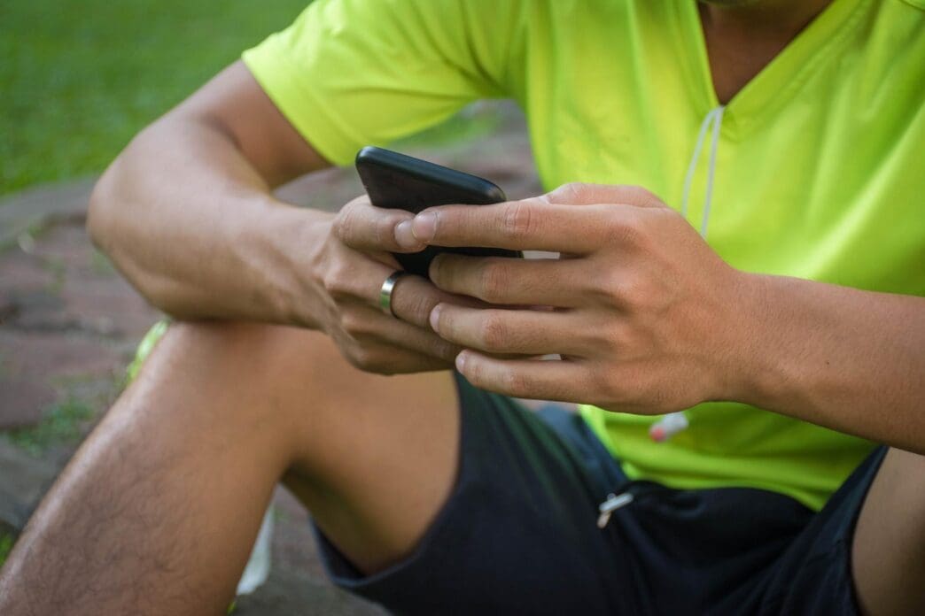 Man's midsection and hands are visible as he uses a mobile phone while seated outside.