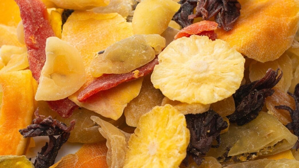 Close-up of a mix of dried exotic fruits including mango slices, pineapple, passion fruit, and papaya.