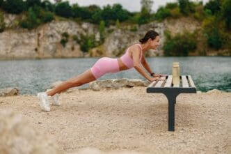 A woman performs pushups on a deck overlooking calm water.