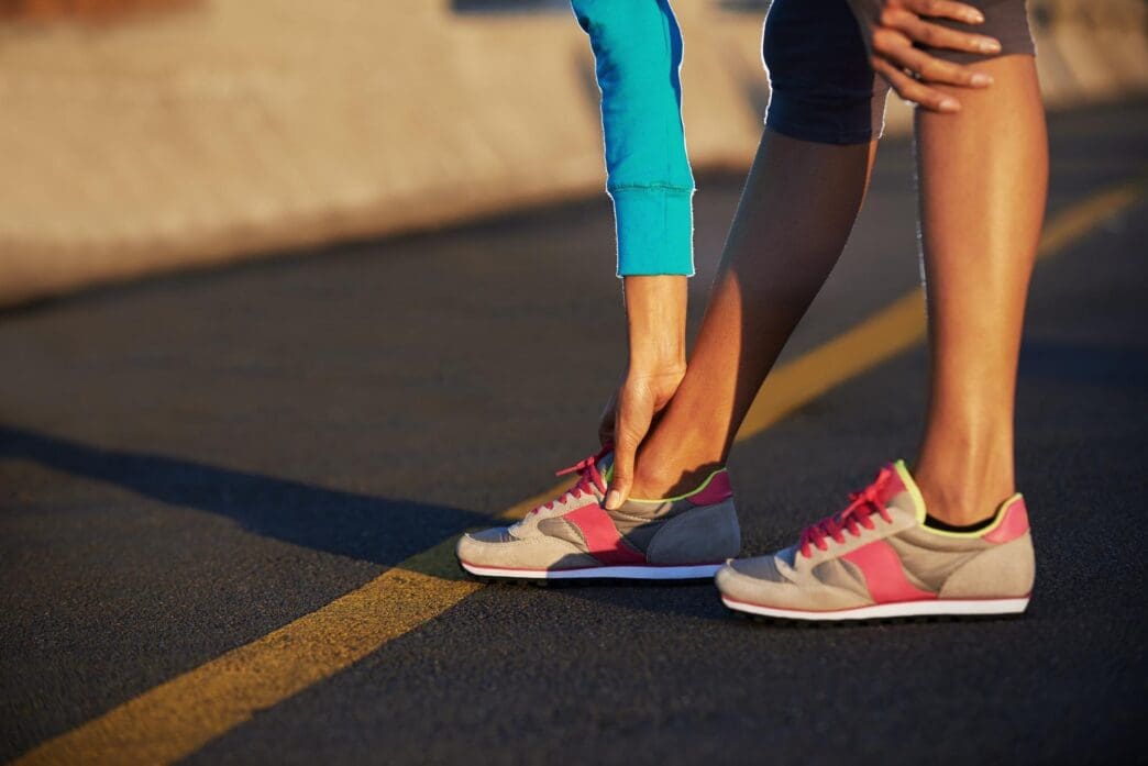 Person in running shoes stretching their legs on a road, preparing for exercise.