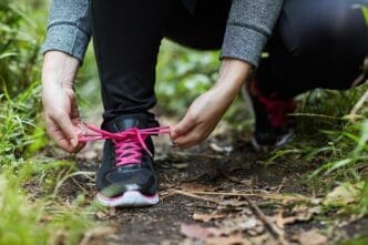 Person tying a shoelace on a sneaker while hiking on a forest trail.