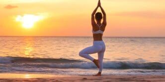 Person in a yoga pose on a sandy beach at sunset.