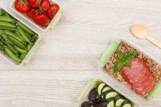 Plastic meal prep containers with portions of buckwheat porridge, meat slices, and green peas.