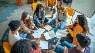 A group of students are gathered, writing lyrics on paper, likely for a song.
