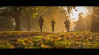 Person running in a sunlit park with colorful autumn leaves.
