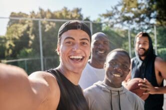 A group of athletes smiles for a selfie on a basketball court after a workout.
