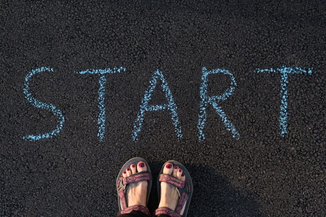 Close-up of a person's feet on pavement next to a white "start" marking, likely indicating the beginning of a race or activity.
