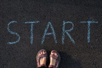 Close-up of a person's feet on pavement next to a white "start" marking, likely indicating the beginning of a race or activity.