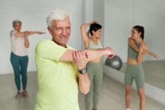 Senior man exercises with other people and an instructor in a gym.