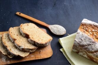 Top-down view of sliced rye bread arranged on a wooden cutting board set on a black table.