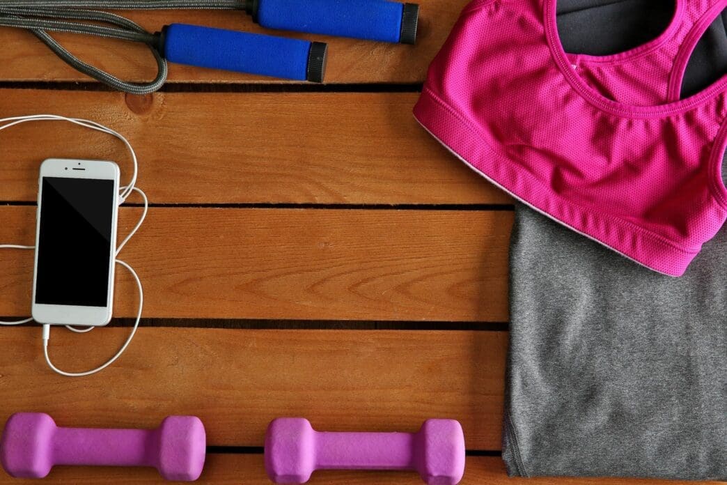 A mobile phone rests on a wooden surface surrounded by athletic equipment and clothing.