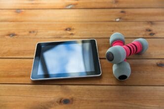 Close-up of dumbbells and a tablet computer on a wooden floor, representing sports, fitness, technology, and objects.