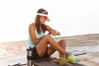 A woman in athletic wear and a cap checks her wristwatch while outdoors.