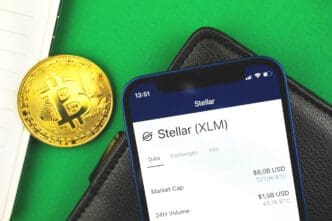 Close-up of the Stellar XLM cryptocurrency logo displayed on a mobile phone screen, with Bitcoin and a business workspace in the background.