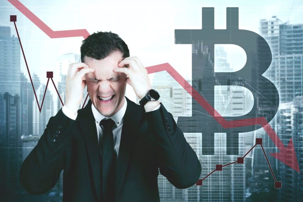 A stressed male manager stands near a declining statistic and a Bitcoin symbol against a modern cityscape background.