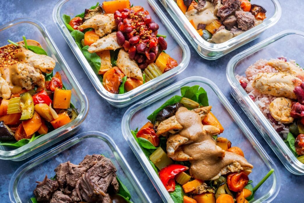 Top-down view of chicken and beef dishes with rice and vegetables displayed in clear containers.