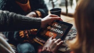 Two hands hold a tablet displaying a donation screen with a heart symbol, suggesting an online charitable contribution.