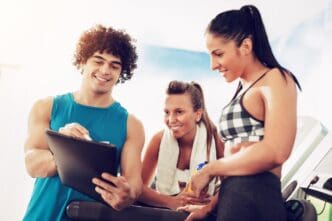 Two women smile while consulting with an instructor at a gym.
