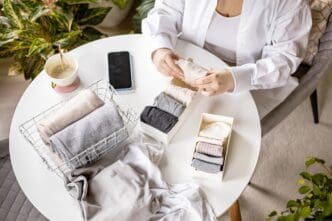 Unrecognizable woman sorts neatly folded white linen cotton textiles at a table with containers and a basket.