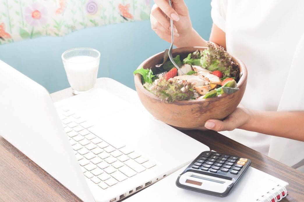 A woman's hand holds a salad bowl while she works, illustrating a healthy lifestyle.