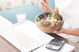 A woman's hand holds a salad bowl while she works, illustrating a healthy lifestyle.