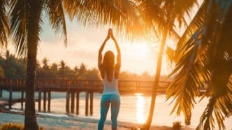 A woman practices yoga on a sandy beach during a sunset.
