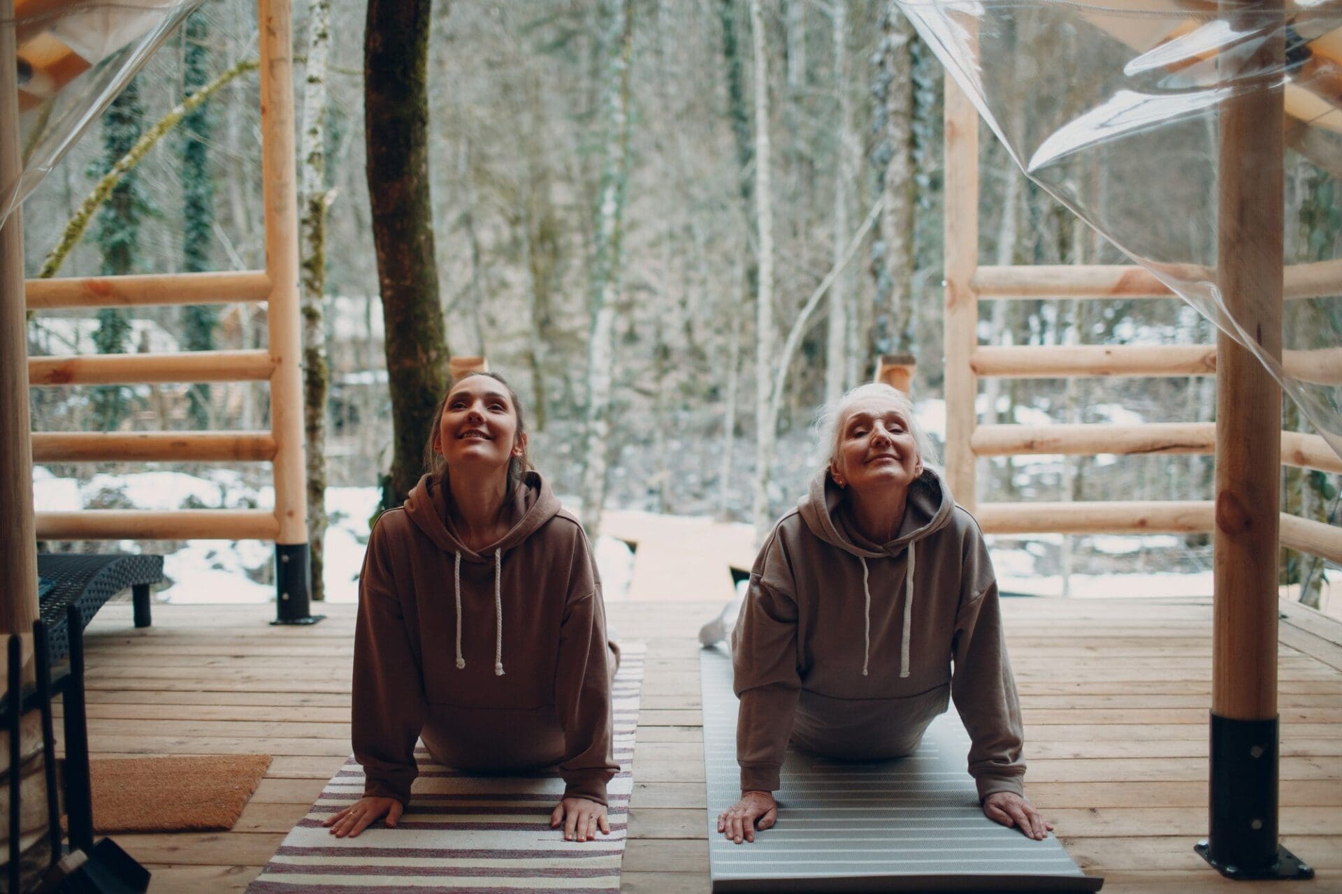 A senior woman and a young woman relax inside a glamping tent, practicing yoga and meditation in a modern, zen-like setting.