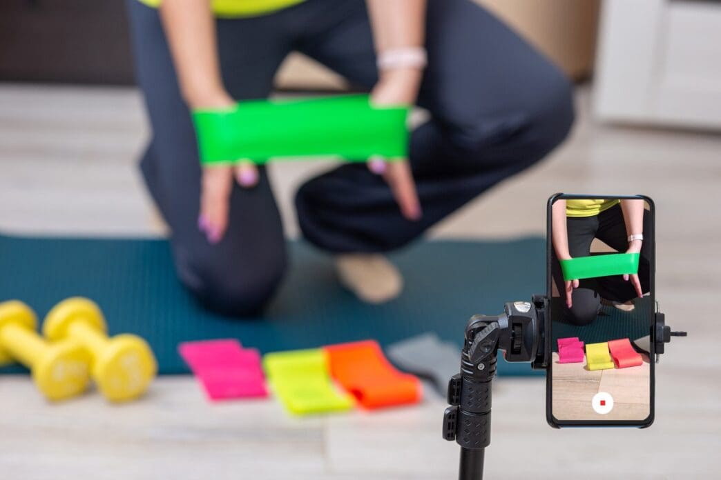 A woman in sportswear demonstrates multi-colored elastic bands in a home setting.